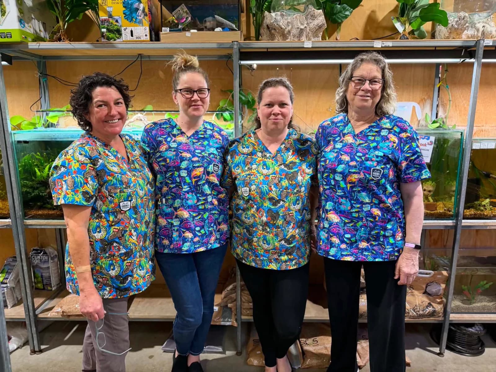 The Erskine Pets team, four staff in matching fish-print scrubs, standing in front of the aquarium racks